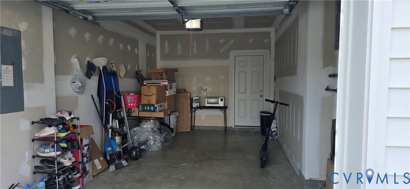 Attached garage featuring an overhead door mechanism, concrete flooring, and an interior access door