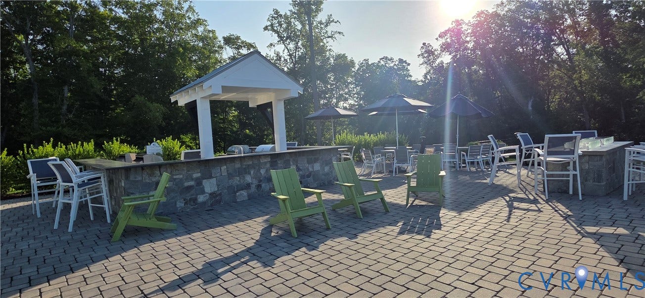 Expansive paver patio featuring a stone-clad outdoor kitchen with a white pergola, multiple seating areas with patio umbrellas, and a built-in stone fire pit