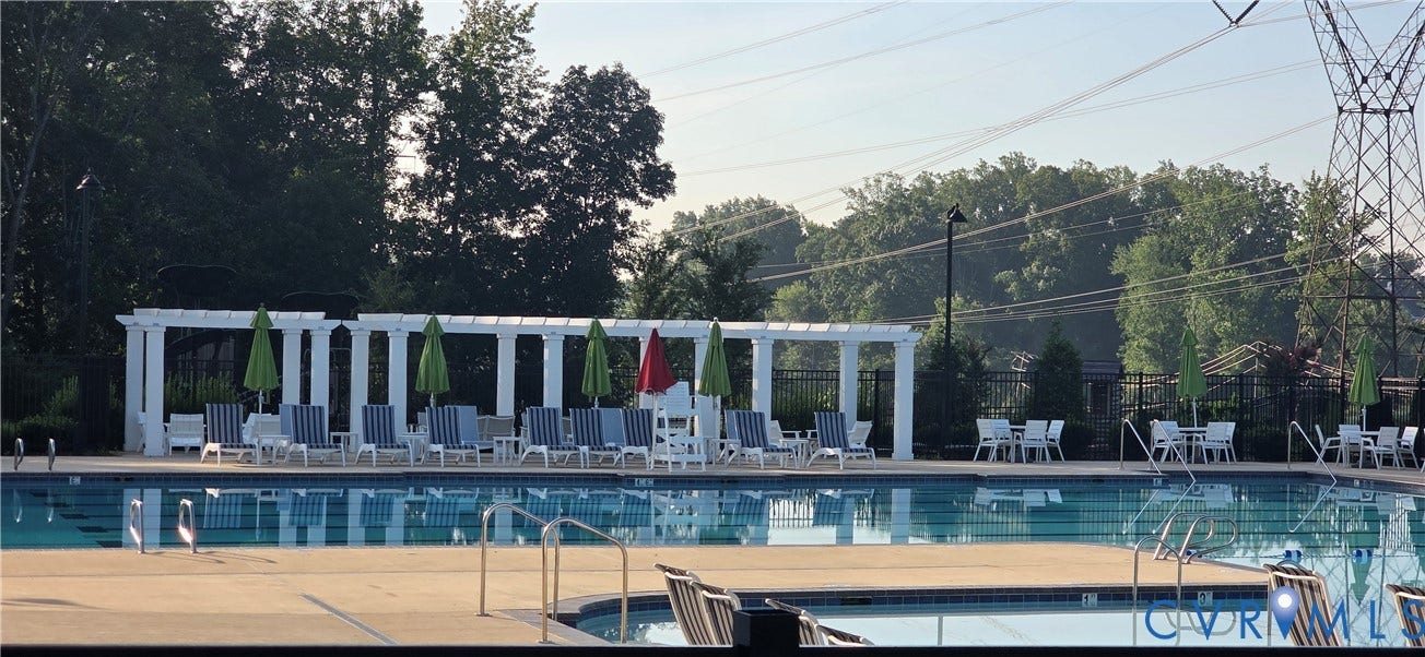 Community swimming pool with integrated spa, surrounded by a concrete deck and framed by a white pergola