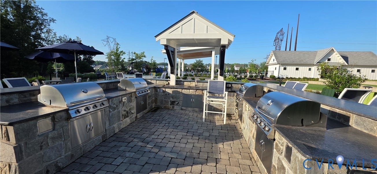 Outdoor grilling station featuring multiple built-in stainless steel grills, stone-finish cabinetry, dark stone countertops, and a paver patio