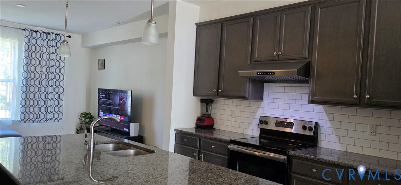Kitchen island with double basin sink, dark wood cabinetry, stainless steel range and hood, subway tile backsplash, and granite countertops