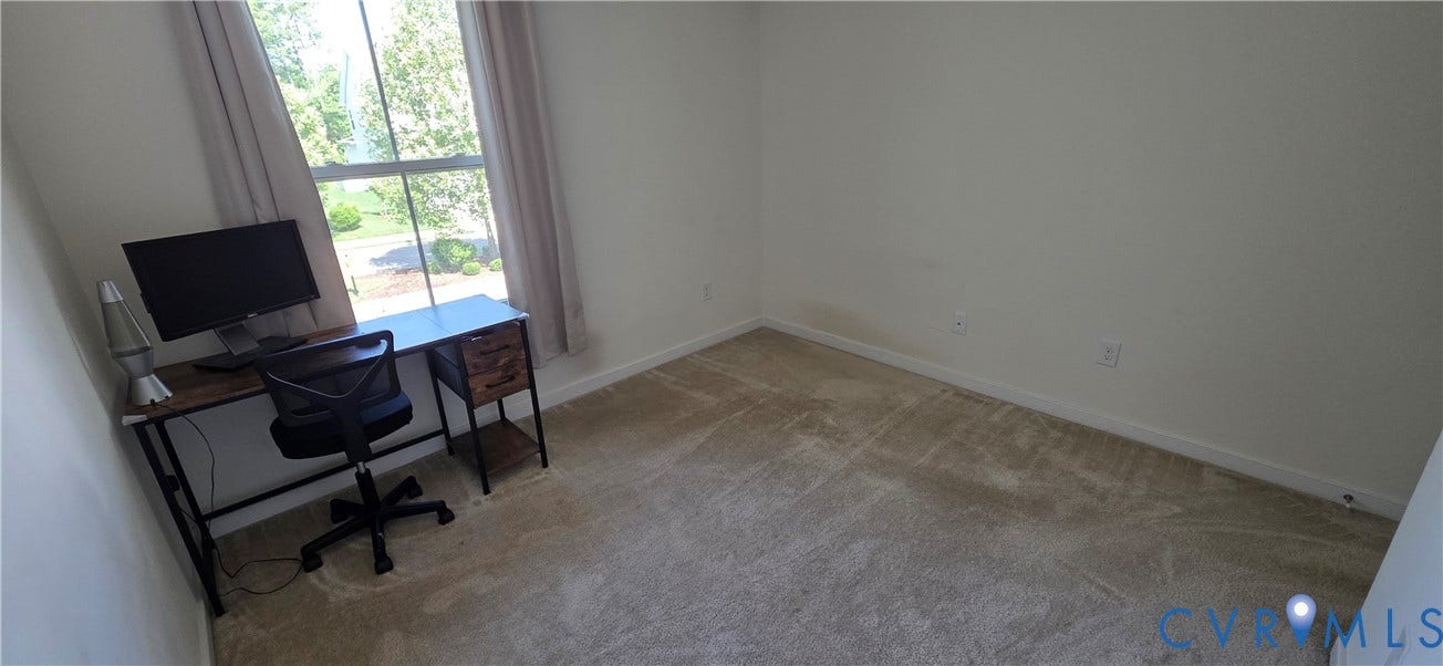 Carpeted room with a window featuring light-colored drapes, white walls, and white baseboards
