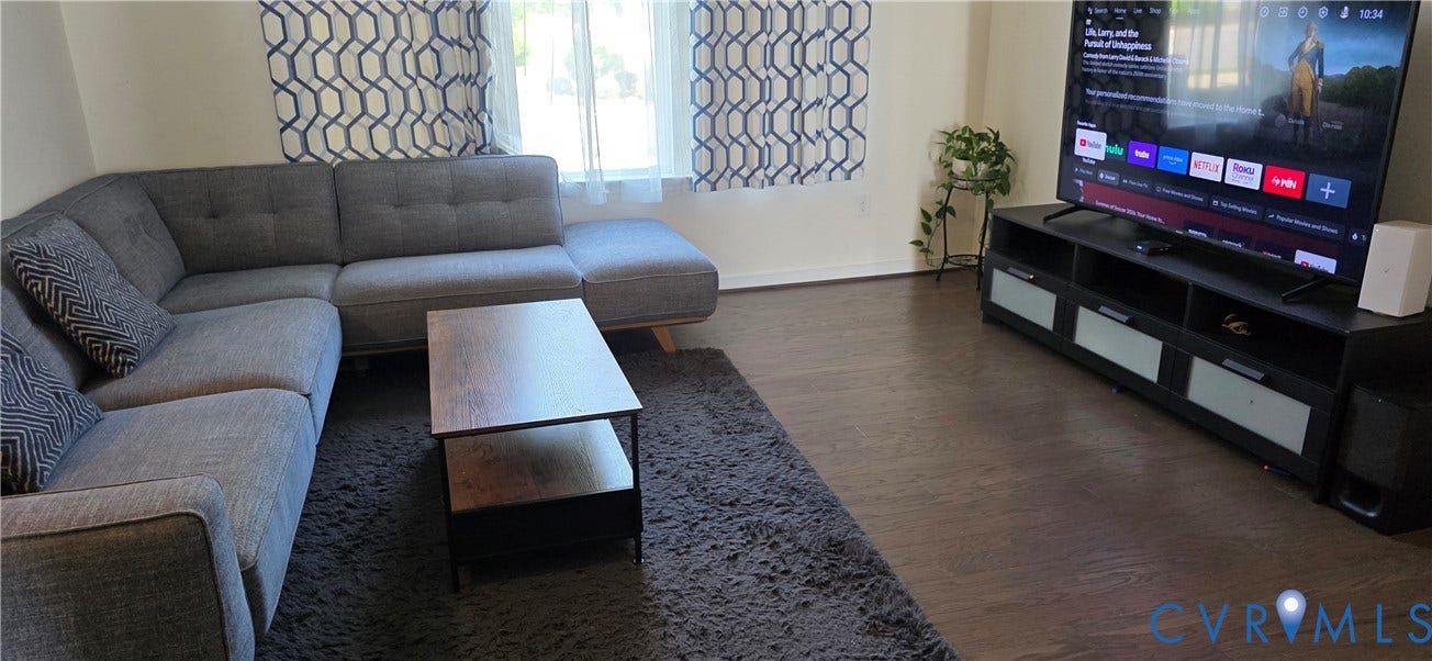 Spacious living area featuring wood-finish flooring, light-colored walls, and large windows