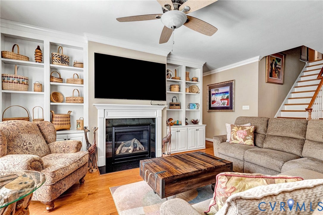 1020 Belva Court, Glen Allen, VA 23059 Living area featuring a central fireplace with a white mantel, built-in shelving, wood-finish flooring, a ceiling fan, and a staircase with white risers and wood treads