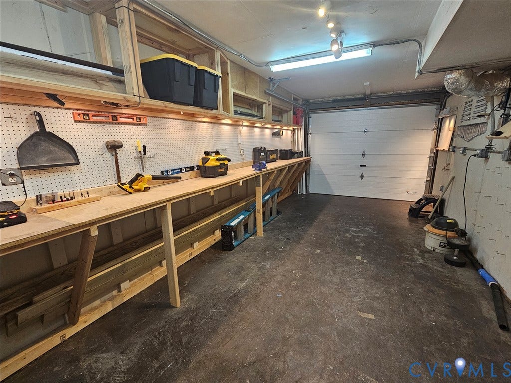 14600 Ramblewood Drive, Chester, VA 23836 Attached garage featuring a workbench, pegboard, overhead storage, concrete flooring, and a roll-up garage door