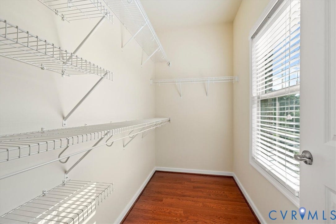 Generous closet space featuring multiple wire shelving units, wood-finish flooring, and a window with blinds