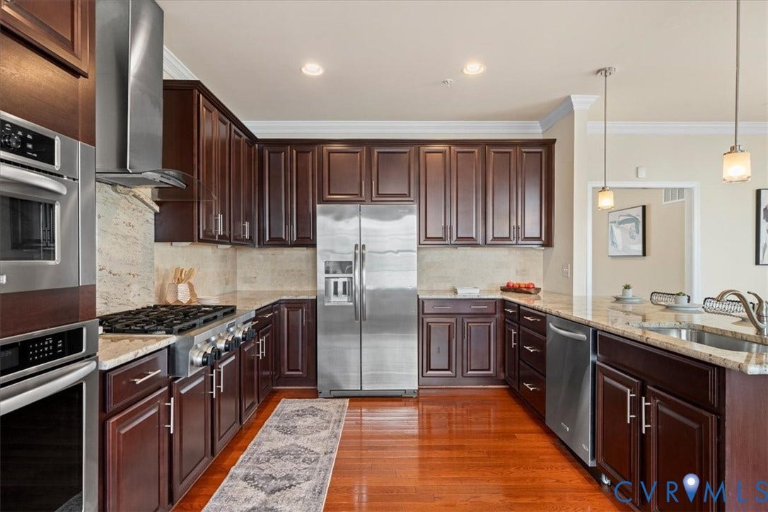 Cherry wood cabinetry, stainless steel appliances, light-toned countertops, and wood-finish flooring
