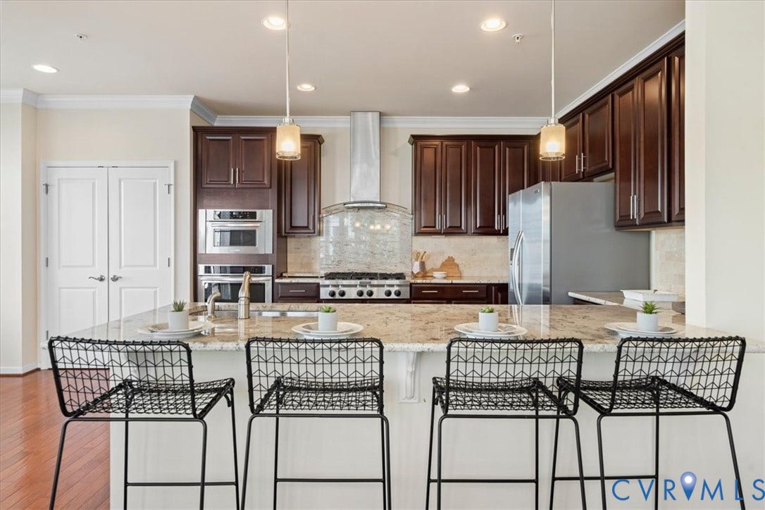 Kitchen featuring dark wood cabinetry, stainless steel appliances, a large island with a stone countertop, and recessed lighting