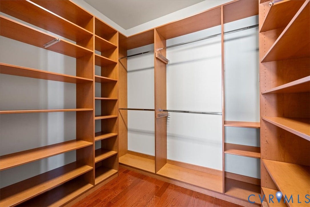Custom closet organization system with wood-finish shelving, multiple hanging rods, and rich wood-finish flooring
