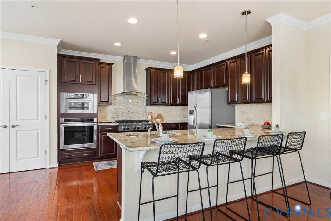 Wood-finish flooring, dark wood cabinetry, stainless steel appliances, pendant lighting, and a granite-finish island