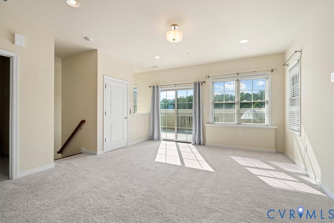 Spacious interior featuring neutral carpet, recessed lighting, a sliding glass door, and multiple windows with blinds