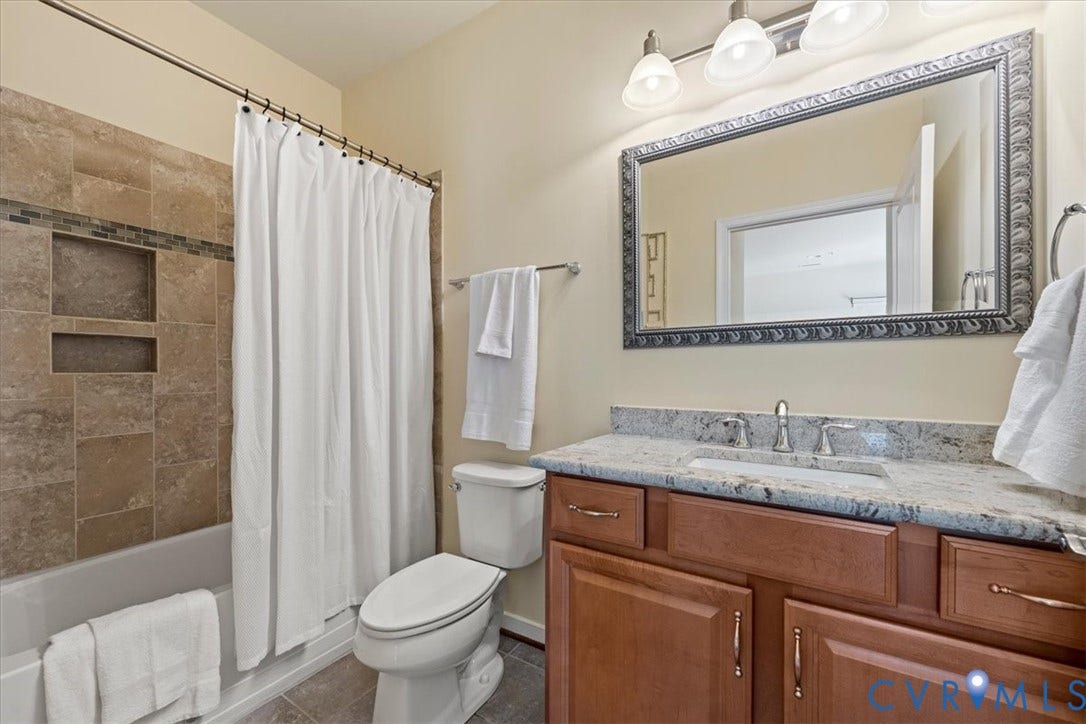 Bathtub with tiled surround and integrated shelving, wood-finish vanity with an undermount sink, and a framed mirror with overhead lighting