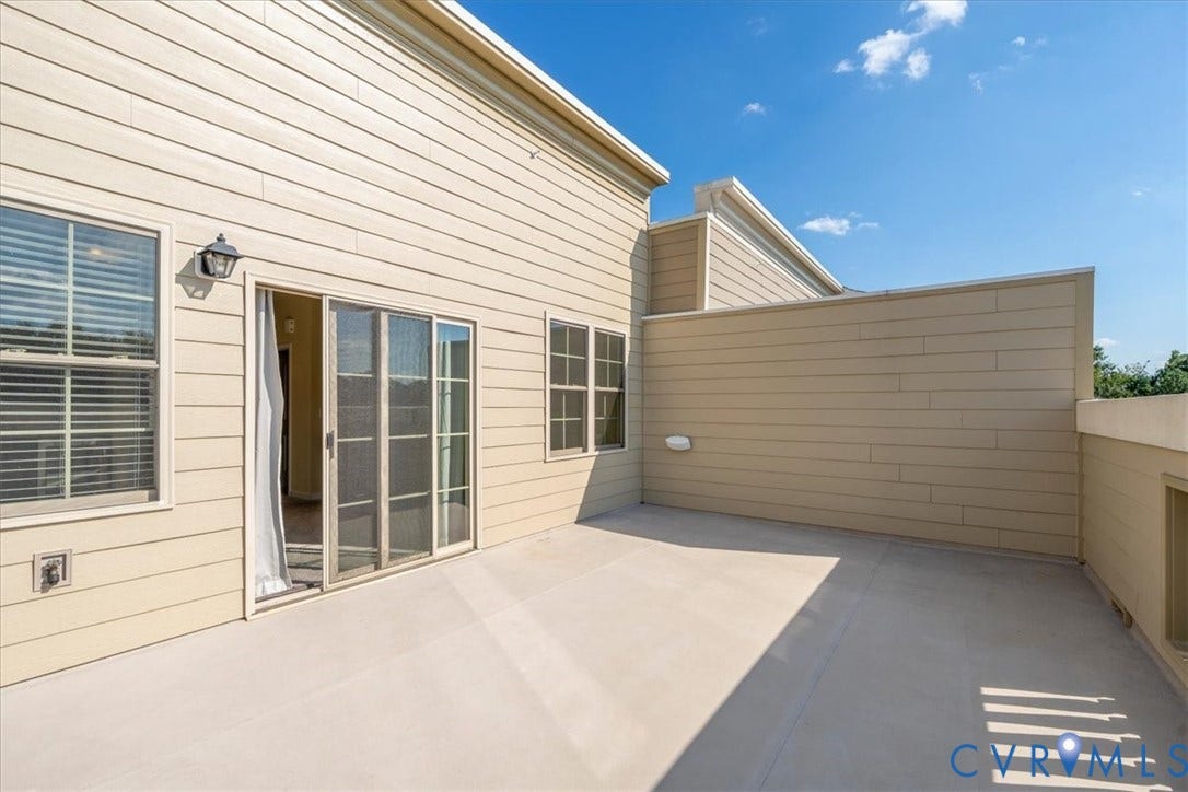 Spacious outdoor balcony with a light-colored solid surface, featuring a sliding glass door entry and multiple windows