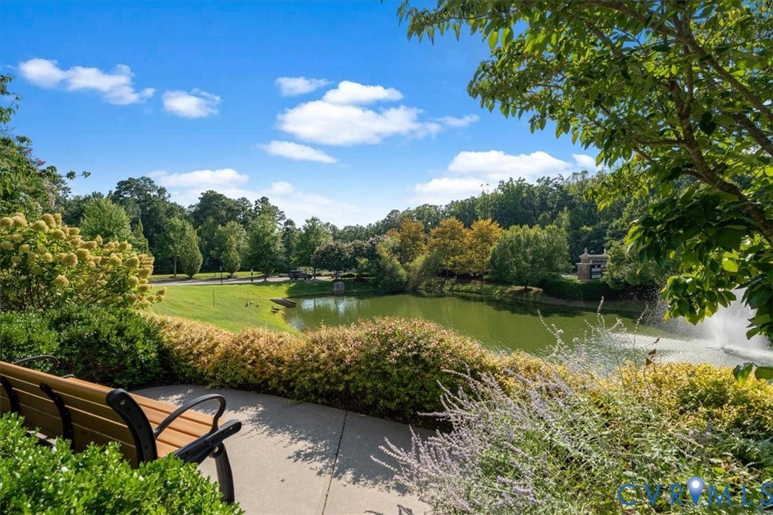 Lush landscaping with a paved pathway, a tranquil pond featuring a fountain, and mature trees