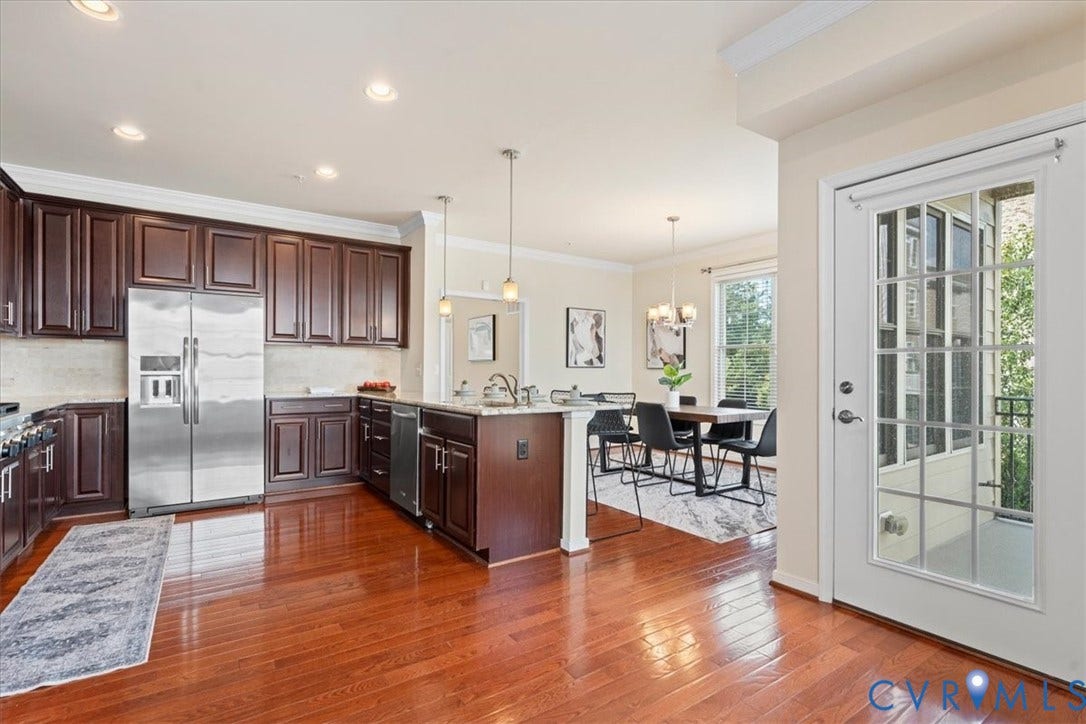 Full kitchen with wood-finish flooring, dark wood cabinetry, stainless steel appliances, and a central island with a sink