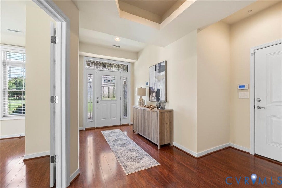 Rich wood-finish flooring with a multi-paneled entry door, transom window, and sidelights