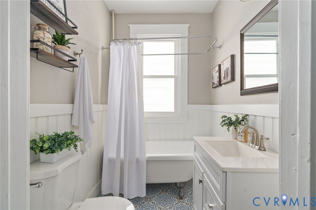 3314 Grayland Avenue, Richmond, VA 23221 Bathroom featuring a clawfoot tub, white wainscoting, patterned floor tiles, a single-sink vanity with a light-toned countertop, and a window providing natural illumination