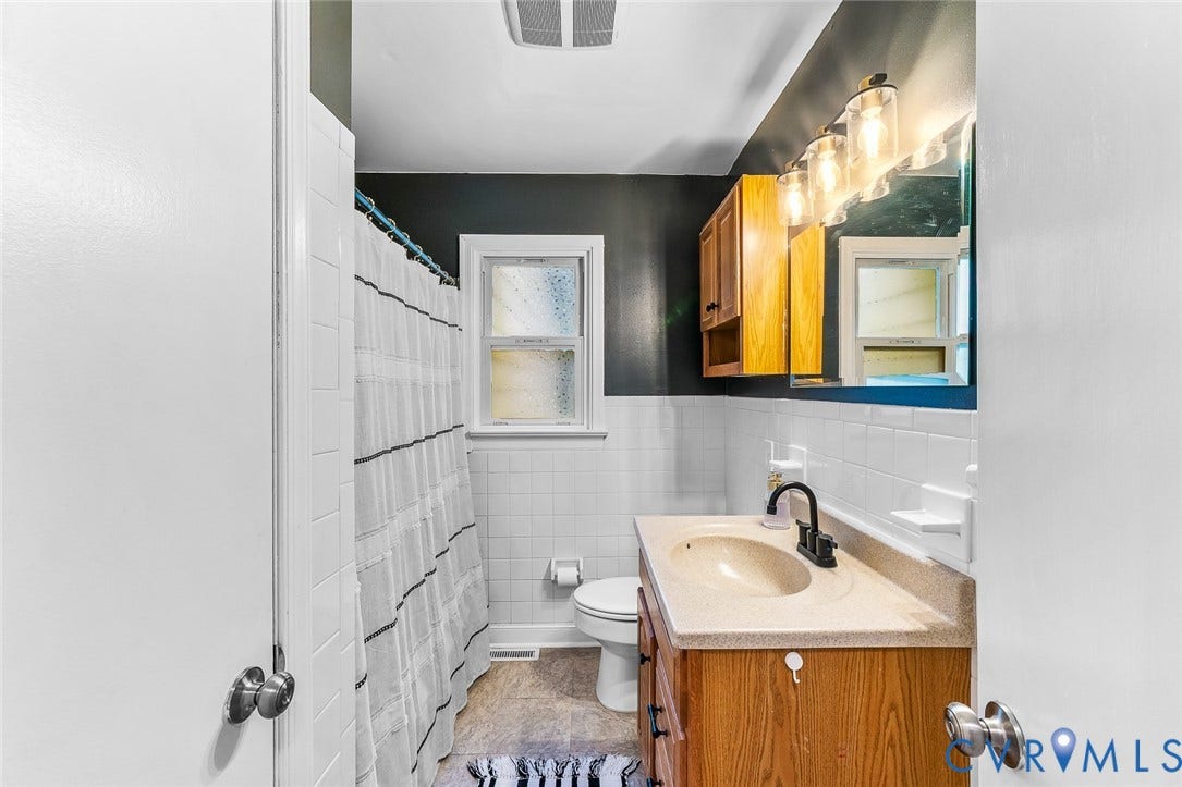 Bathroom featuring a wood vanity with integrated sink, white tiled walls, a window, and overhead lighting