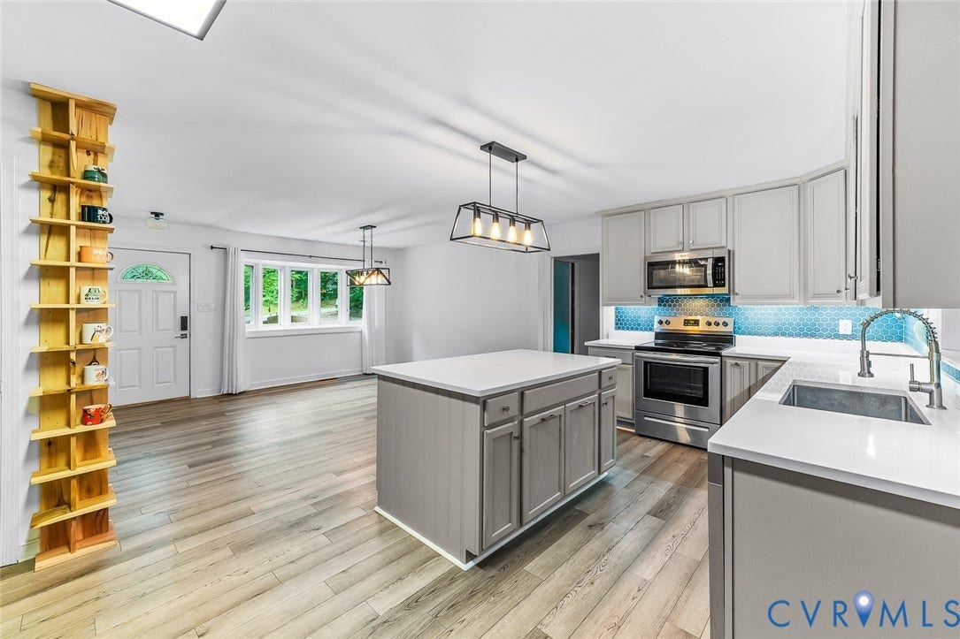 Open-concept kitchen featuring an island, light gray cabinetry, stainless steel appliances, and a blue tile backsplash