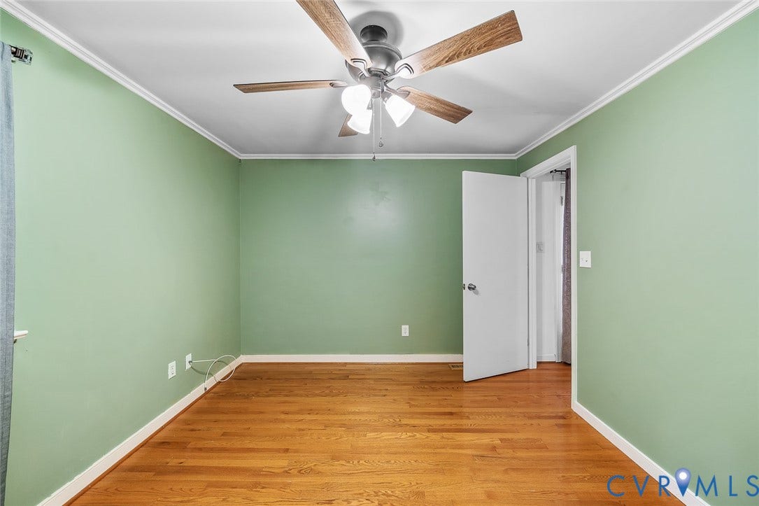 Room featuring wood-finish flooring, light green walls, white crown molding, and a ceiling fan with light fixture