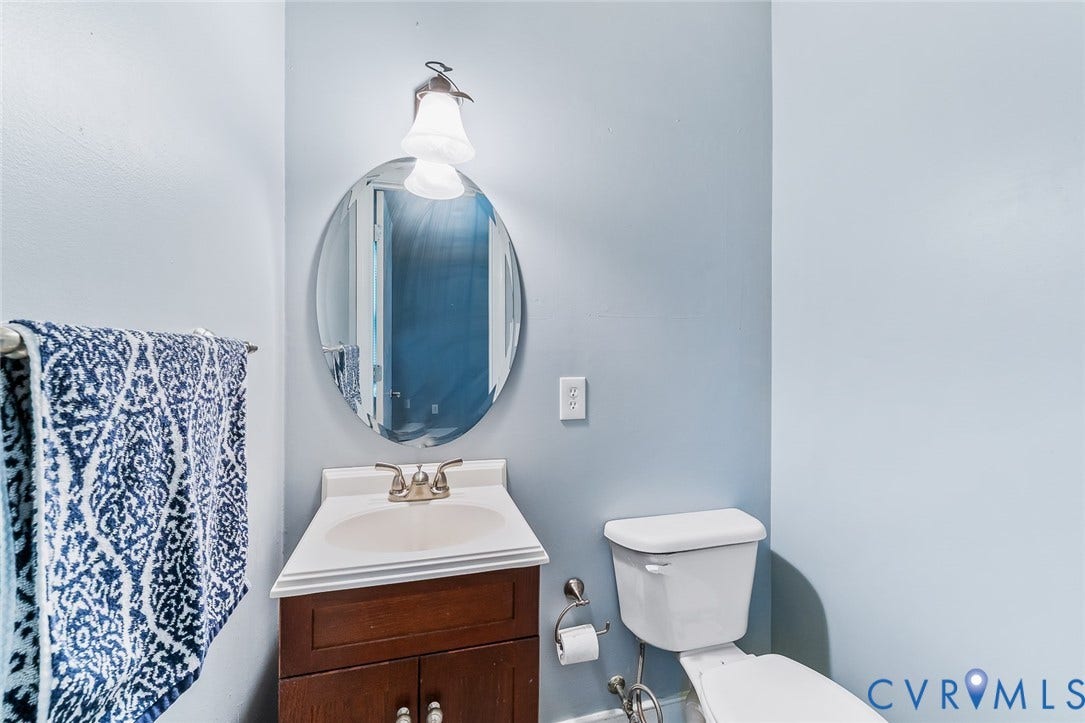 Powder room featuring a single-sink vanity with wood-finish cabinetry, a coordinating oval mirror, and an overhead vanity light fixture