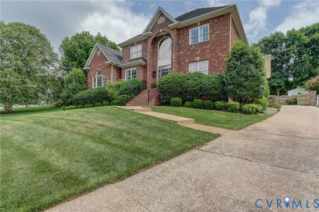 332 Rexmoor Terrace, Richmond, VA 23236 Brick facade residence featuring a prominent arched window, multi-pane windows, mature landscaping, and an integrated concrete driveway