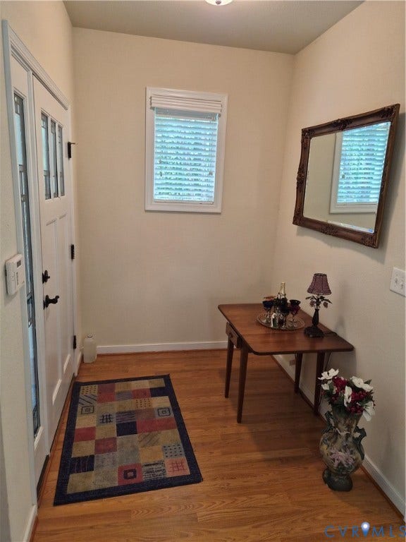 Entryway featuring wood-finish flooring, a white paneled door with glass inserts, and a window with blinds