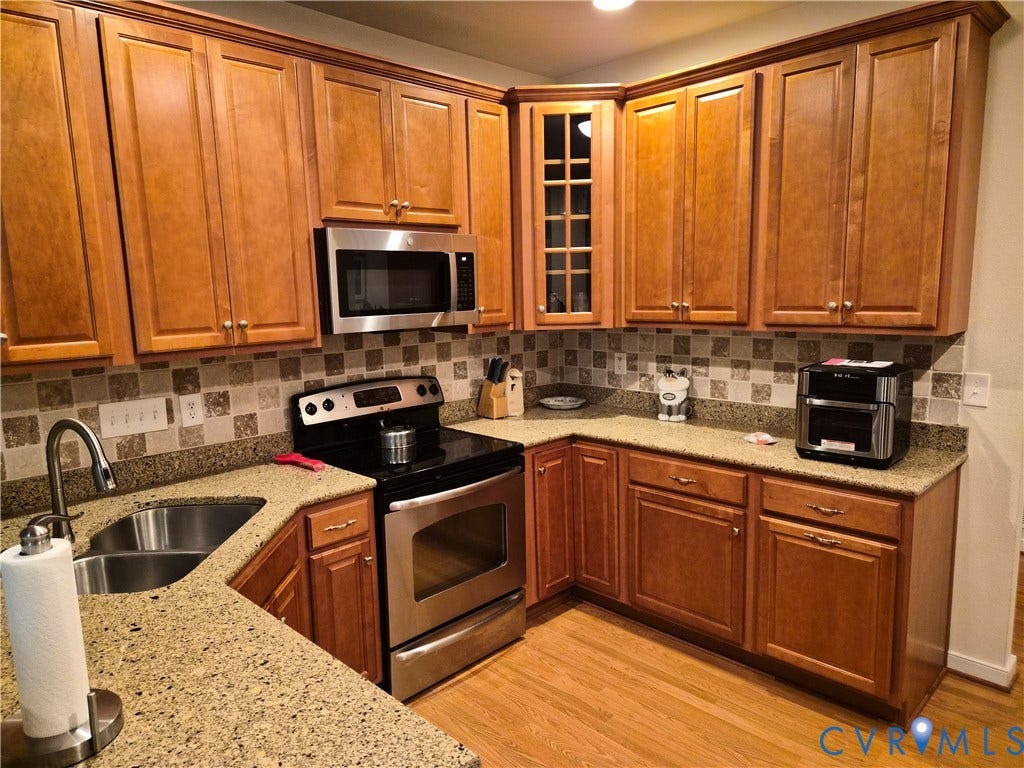 Kitchen featuring wood-finish cabinetry, granite-style countertops, stainless steel appliances, a mosaic tile backsplash, and a double-basin sink