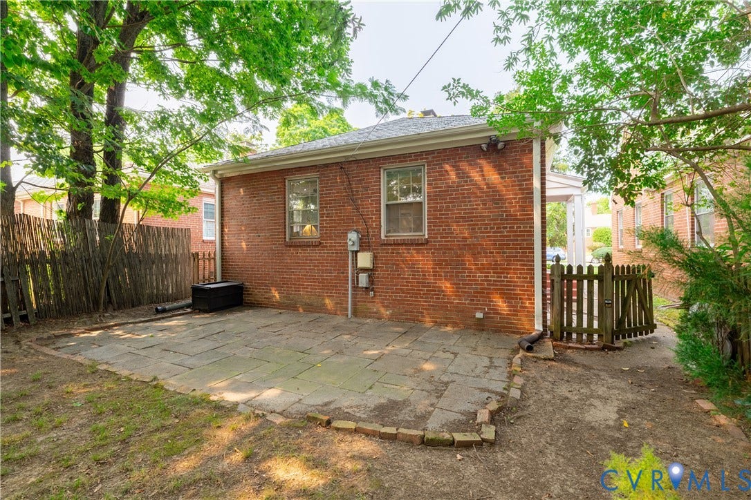 3903 Floyd Avenue, Richmond, VA 23221 Brick exterior with a stone patio, enclosed by a wooden fence and gate, featuring mature trees