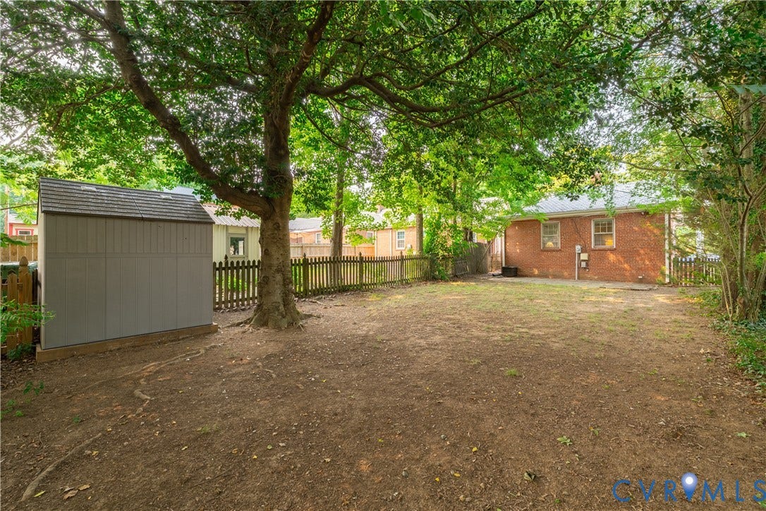 3903 Floyd Avenue, Richmond, VA 23221 Expansive backyard featuring a mature tree, a grey storage shed with a shingled roof, and a wooden picket fence
