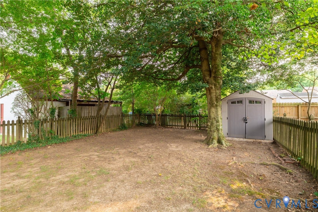 3903 Floyd Avenue, Richmond, VA 23221 Spacious backyard featuring a storage shed with double doors, mature trees, and natural ground cover