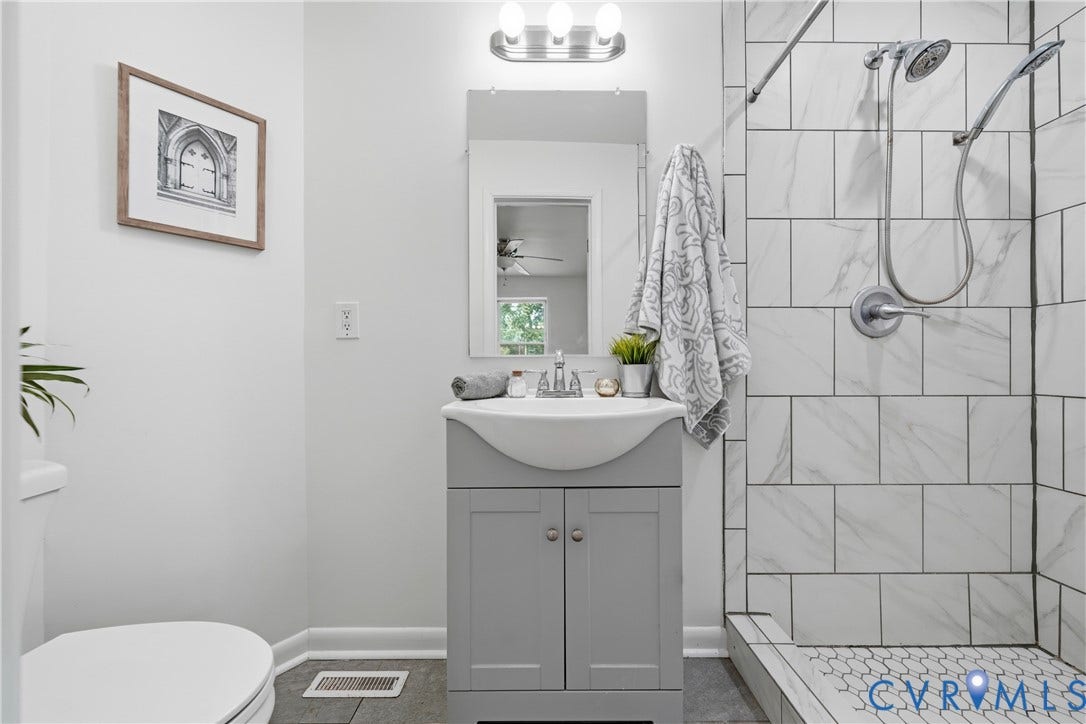 1214 Southbury Avenue, Henrico, VA 23231 Bathroom featuring a light gray vanity with an integrated sink, a tiled shower with a dual showerhead, gray floor tiles, and bright white wall paint