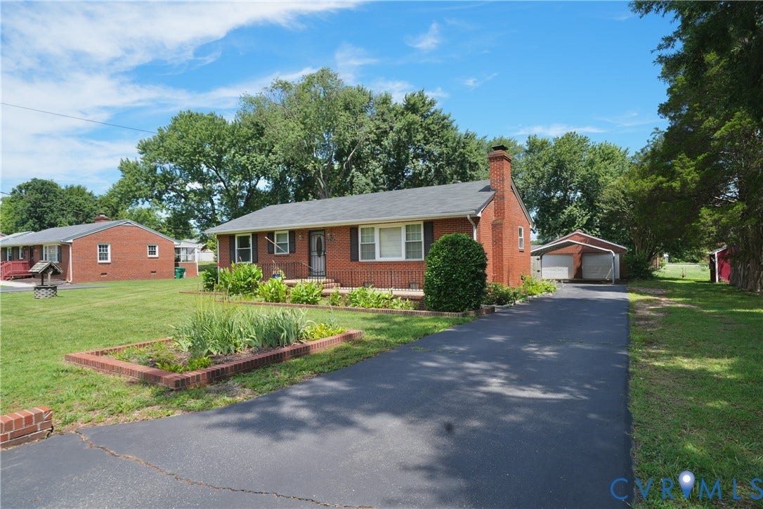 1214 Southbury Avenue, Henrico, VA 23231 Brick exterior residence featuring a dark asphalt driveway, a front yard with a raised garden bed, a covered carport, and mature trees