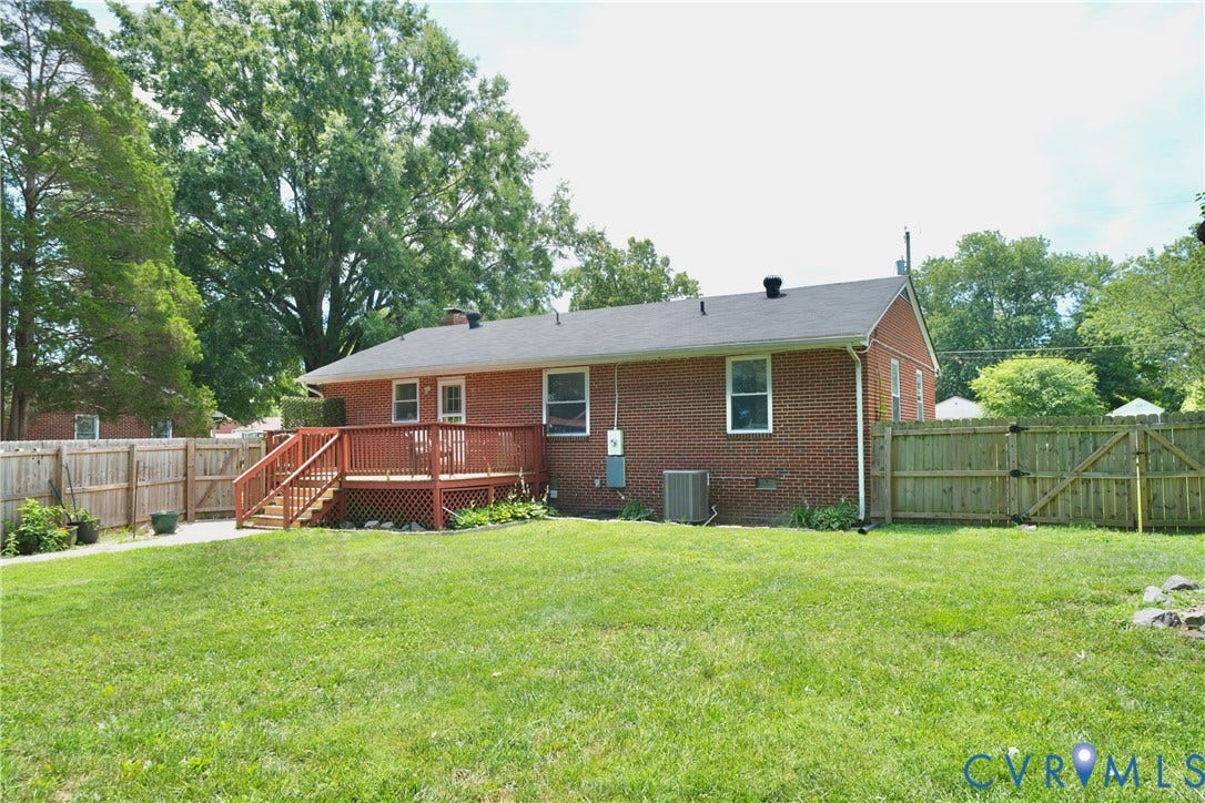 1214 Southbury Avenue, Henrico, VA 23231 Expansive grassy yard featuring a wood privacy fence, a red brick exterior, a dark shingle roof, a wood deck with railings and steps, and mature trees