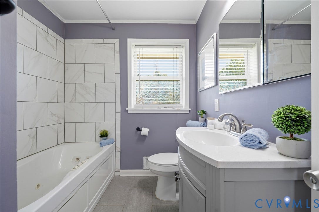 1214 Southbury Avenue, Henrico, VA 23231 Bathroom featuring a white jetted bathtub with a subway tile surround, a single vanity with a white countertop and basin sink, a wall-mounted mirror, and a window with white blinds