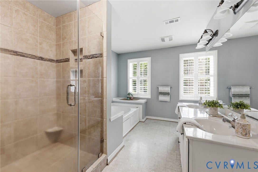 Bathroom featuring a glass-enclosed shower with tile surround, a built-in tub, dual vanity with undermount sinks, and windows with plantation shutters
