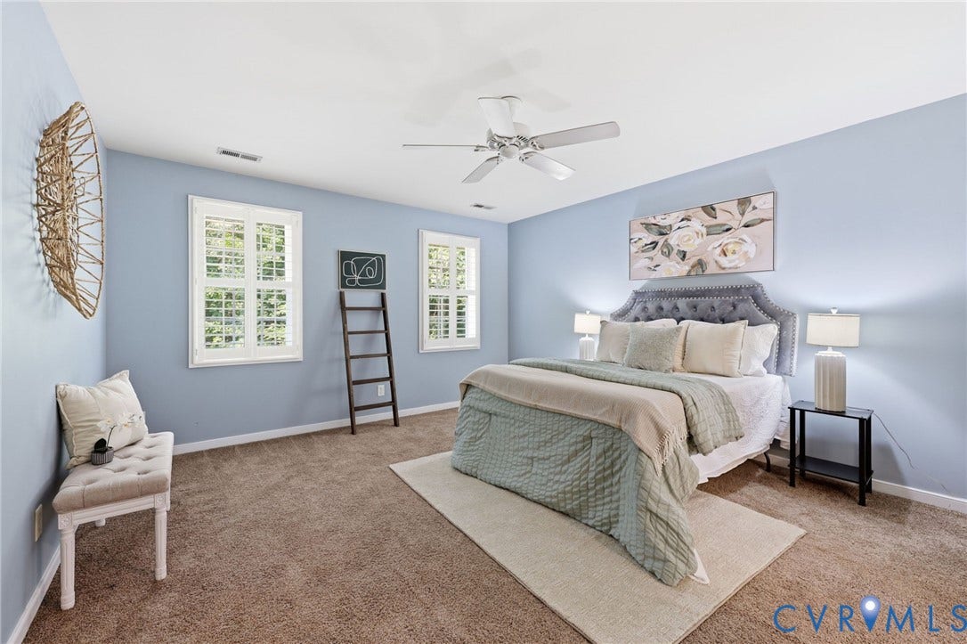 Carpeted bedroom featuring light blue walls, two windows with white trim, and a ceiling fan