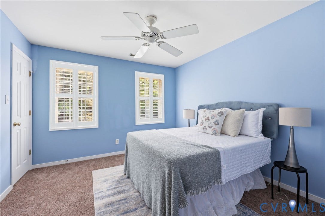 Bright room featuring two windows with white plantation shutters, neutral carpet, and a ceiling fan with light fixture