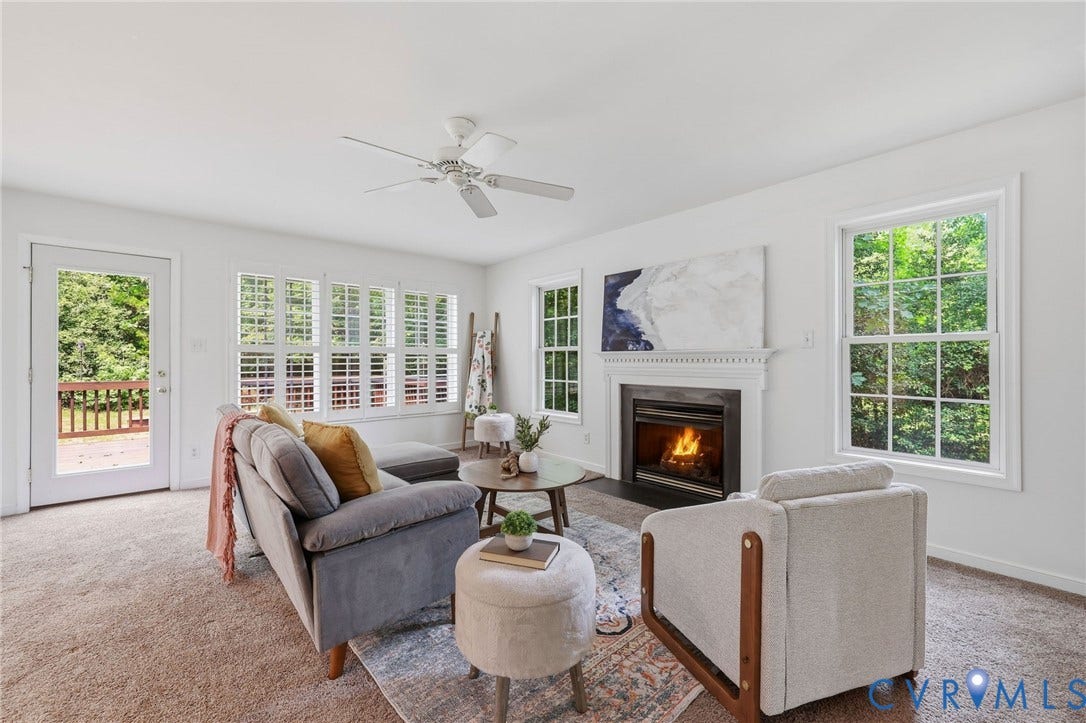 Living area featuring a fireplace with a white mantel, multiple windows, a ceiling fan, and access to an outdoor deck