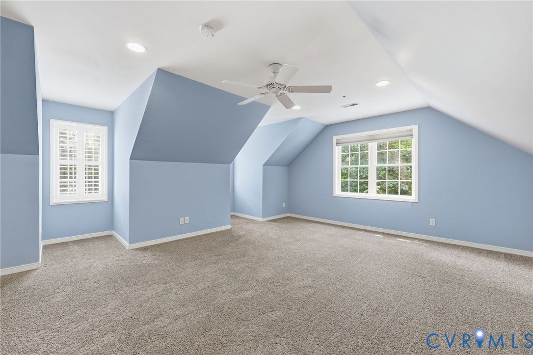 Spacious room featuring sloped ceilings, recessed lighting, and soft gray carpeting