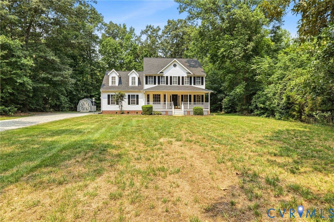 White two-story residence featuring a covered front porch with white columns and railings, dormer windows, and dark shutters