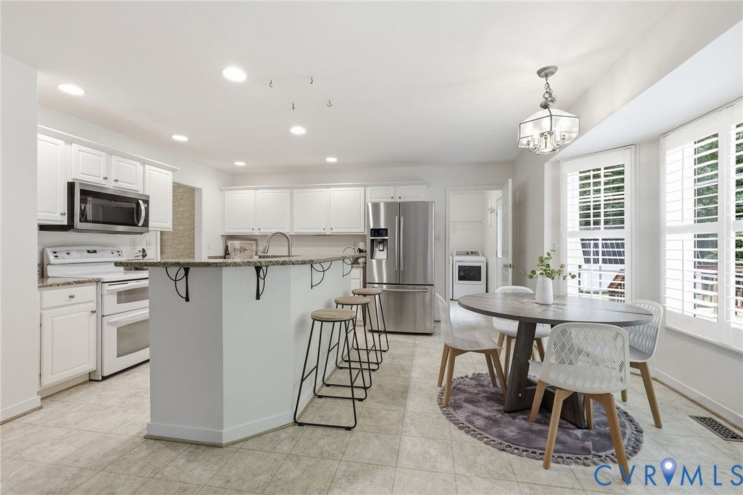Bright kitchen featuring white cabinetry, stone countertops, stainless steel appliances, a center island with seating, and tile flooring