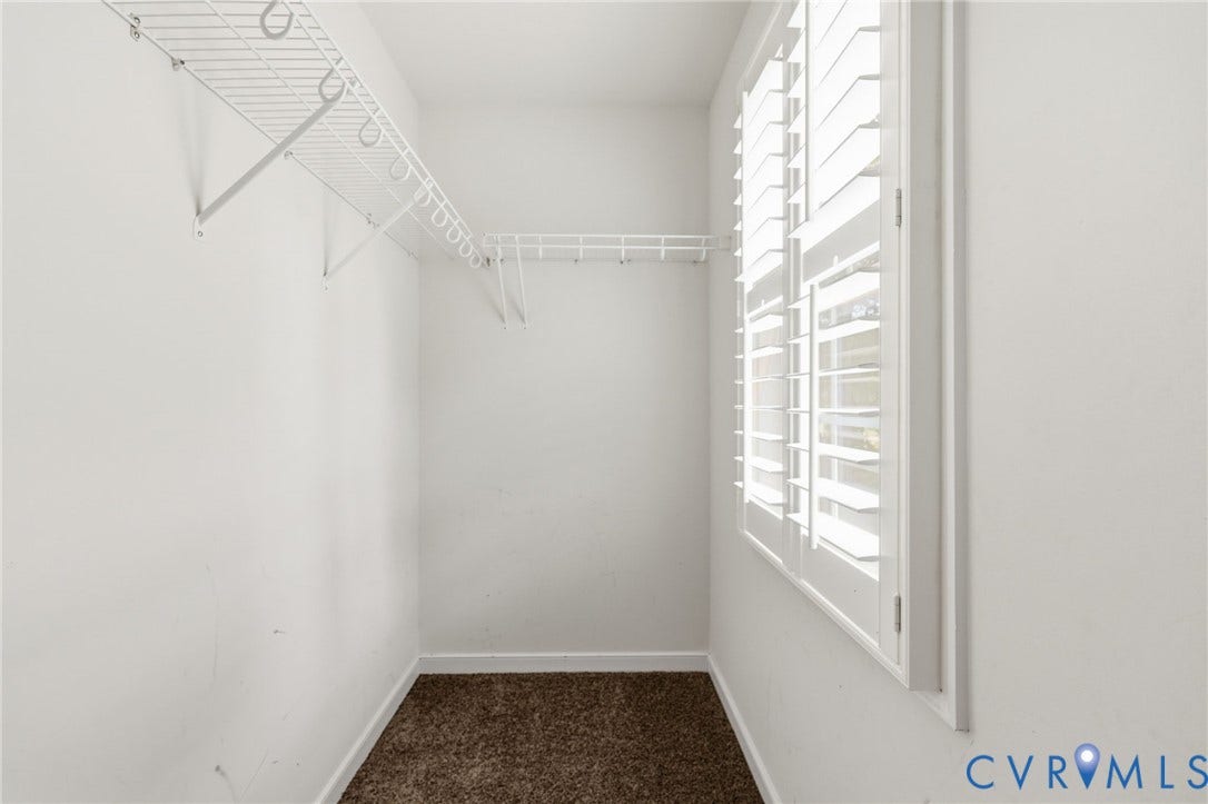 Walk-in closet featuring white wire shelving, plantation shutters, white baseboards, and brown carpet flooring