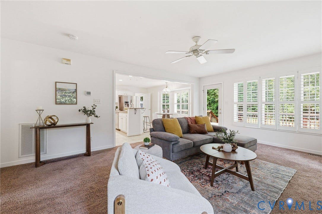Bright living area featuring plush carpeting, a ceiling fan, and white plantation shutters