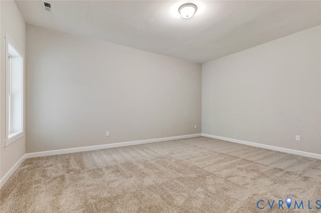 Spacious room featuring neutral carpeting, light-colored walls, white baseboards, and a single window with white trim