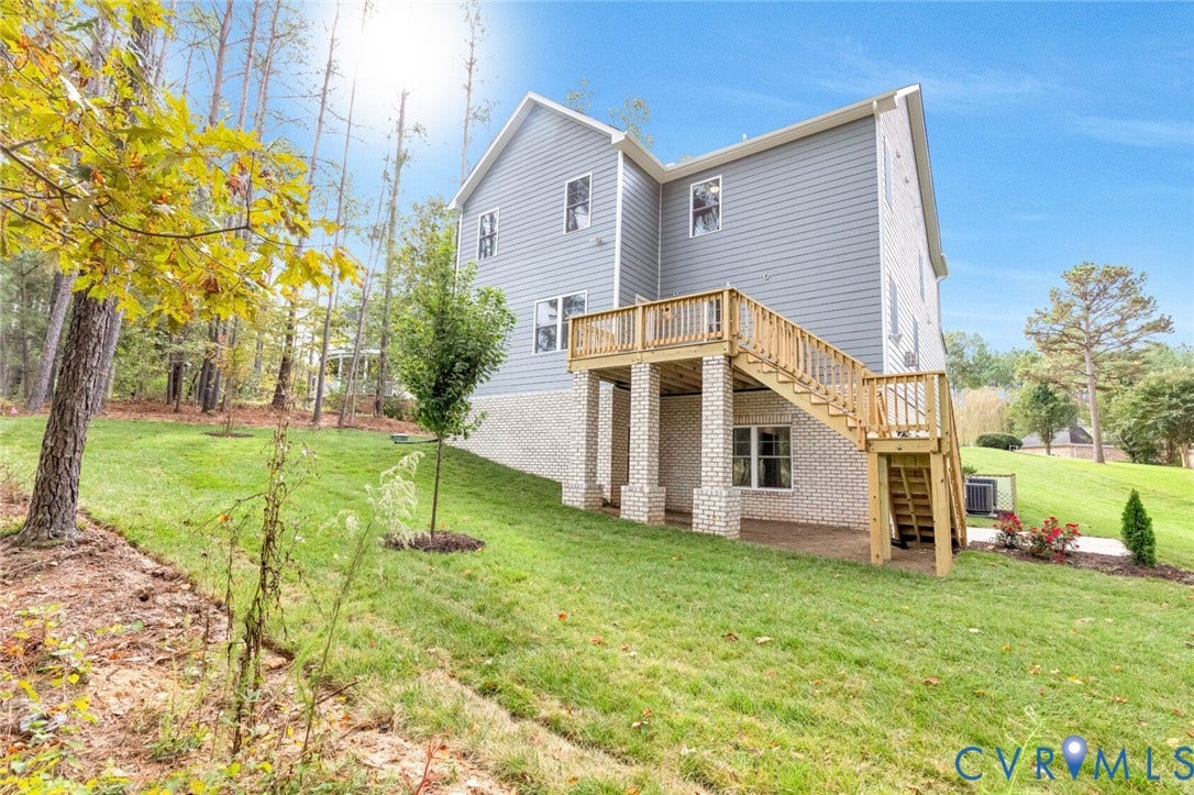 Rear exterior featuring light gray siding, white brick foundation, and an elevated wood deck with stairs to grade