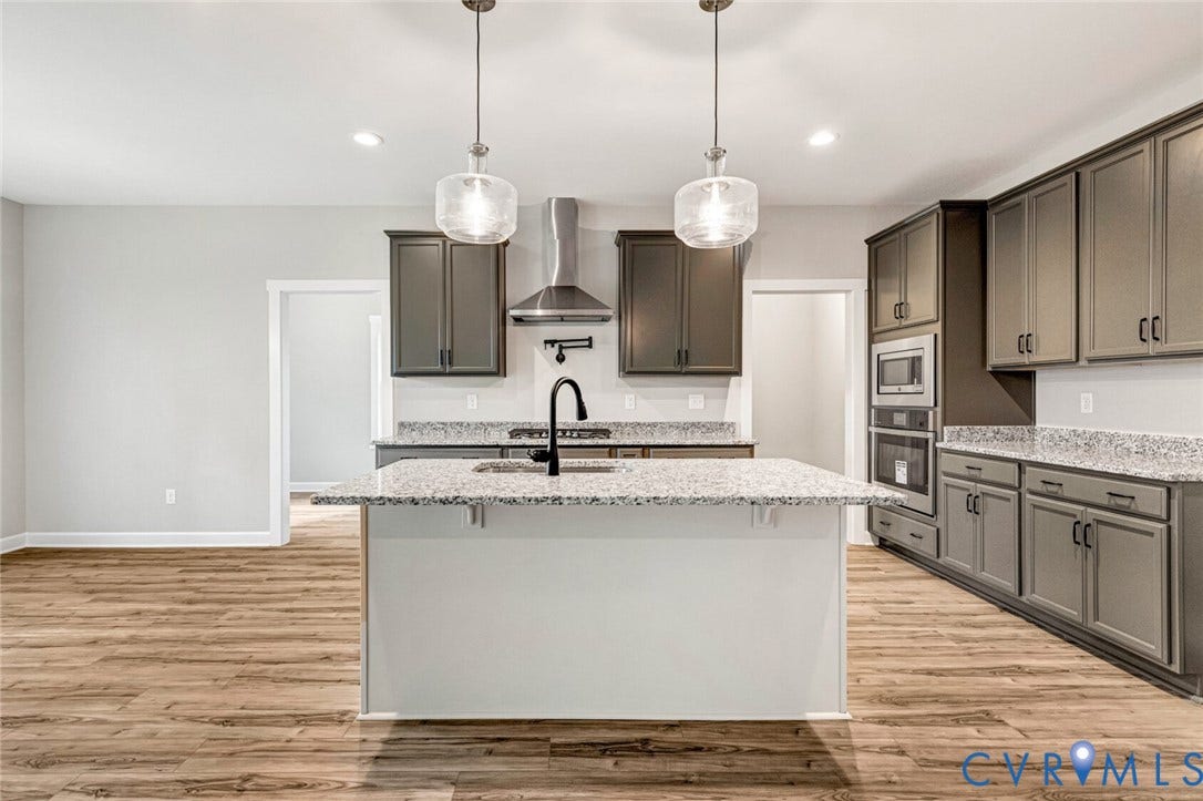 Modern kitchen featuring a central island with an undermount sink and black faucet, light-toned granite countertops, dark gray cabinetry, stainless steel appliances, and wood-finish flooring