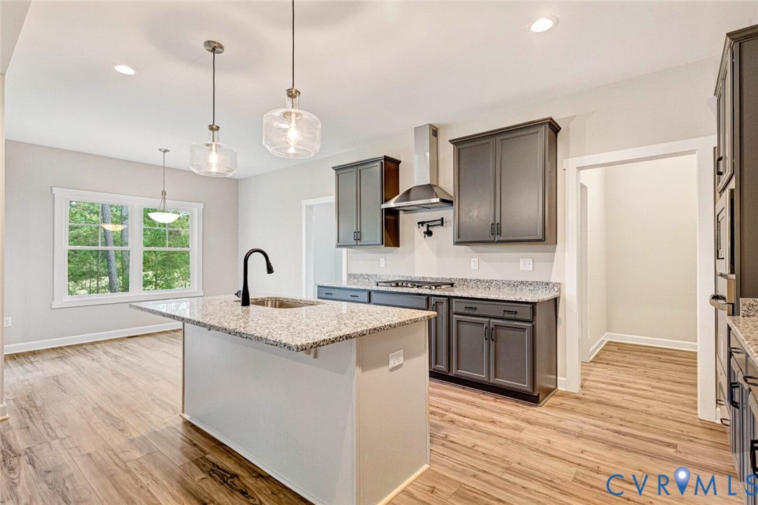 Modern kitchen featuring a spacious island with a sink and gooseneck faucet, light granite countertops, dark cabinetry, and wood-finish flooring