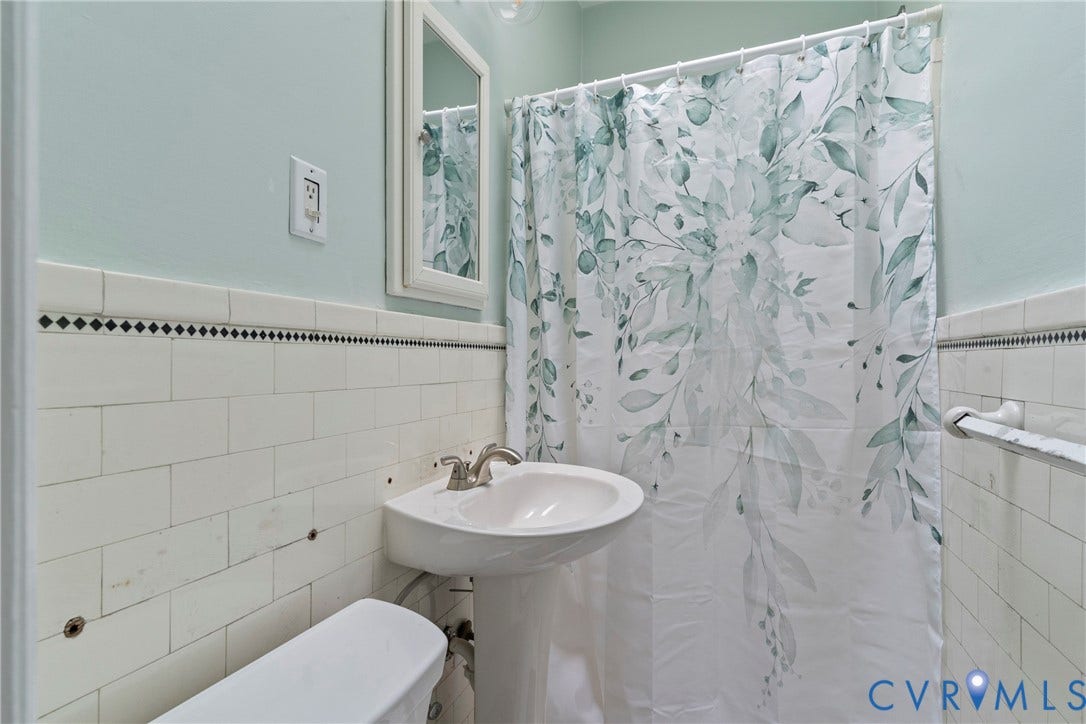 3331 W Grace Street, Monument Avenue, Richmond, VA 23221 Pedestal sink with a polished chrome faucet, white subway tile wainscoting featuring a decorative black and white border, and a framed wall mirror