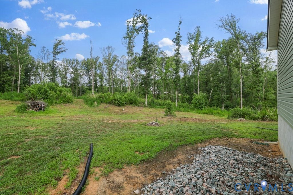 3259 Three Bridge Road, Powhatan, VA 23139 Expansive rear property featuring a sloped, partially cleared landscape, natural tree line, light green siding, and a gravel perimeter